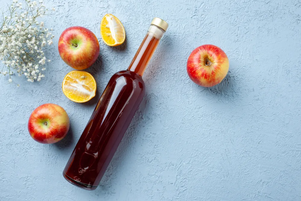 Flasche Apfelessig neben Äpfeln auf hellem Grund