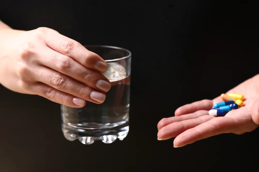 Hand mit Tabletten neben einem Glas Wasser